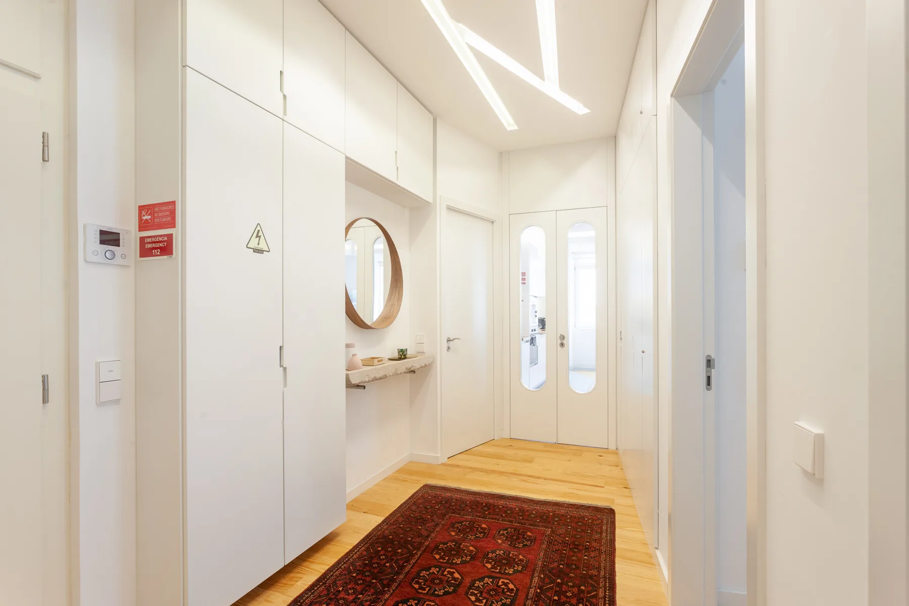Un pasillo luminoso con puertas blancas, suelo de madera y una alfombra estampada.