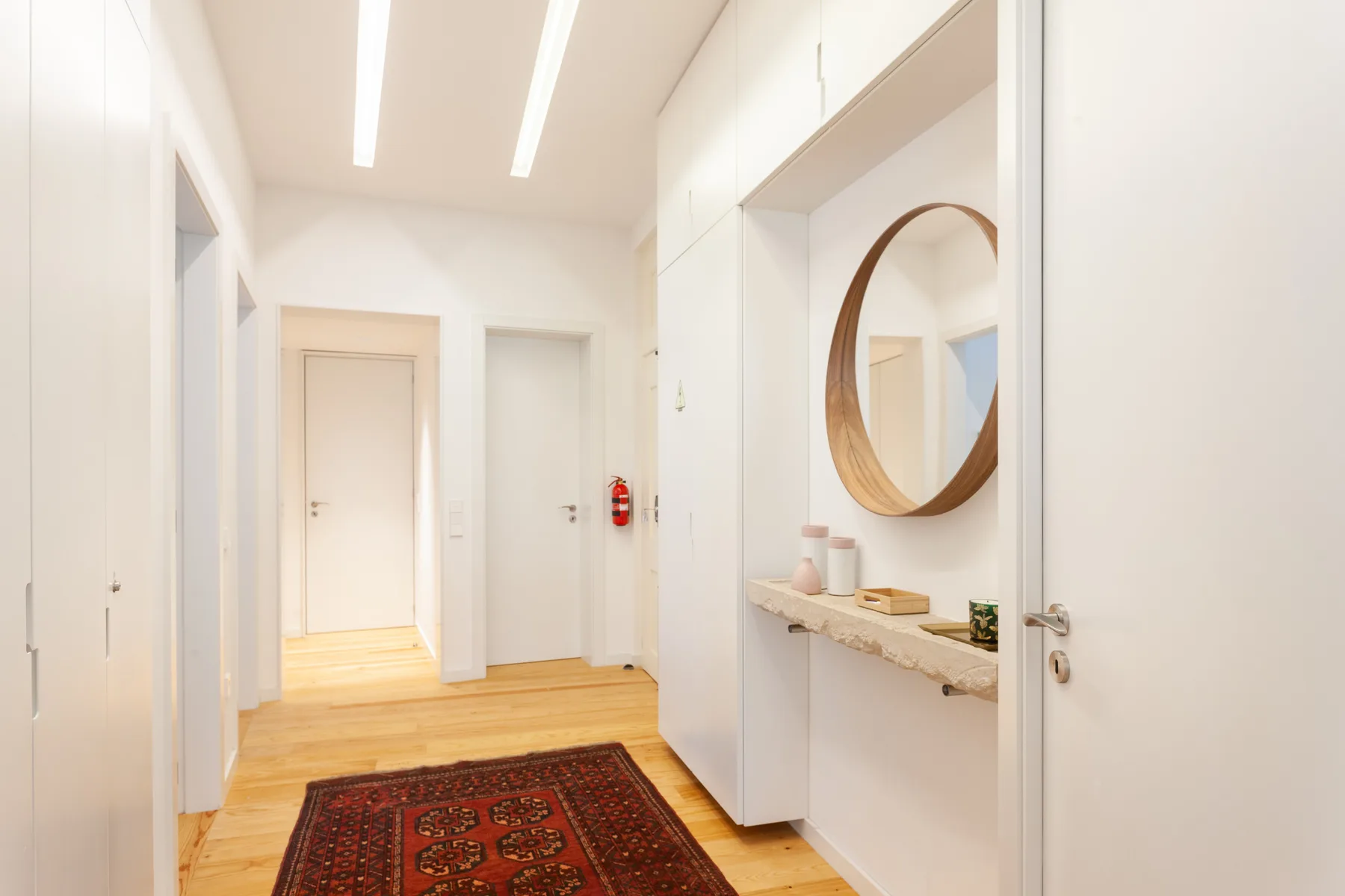 Un pasillo luminoso con suelo de madera y una alfombra roja estampada.