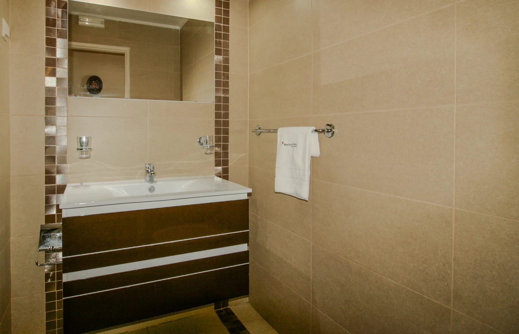 A tiled bathroom with a sink, mirror, and towel rail.