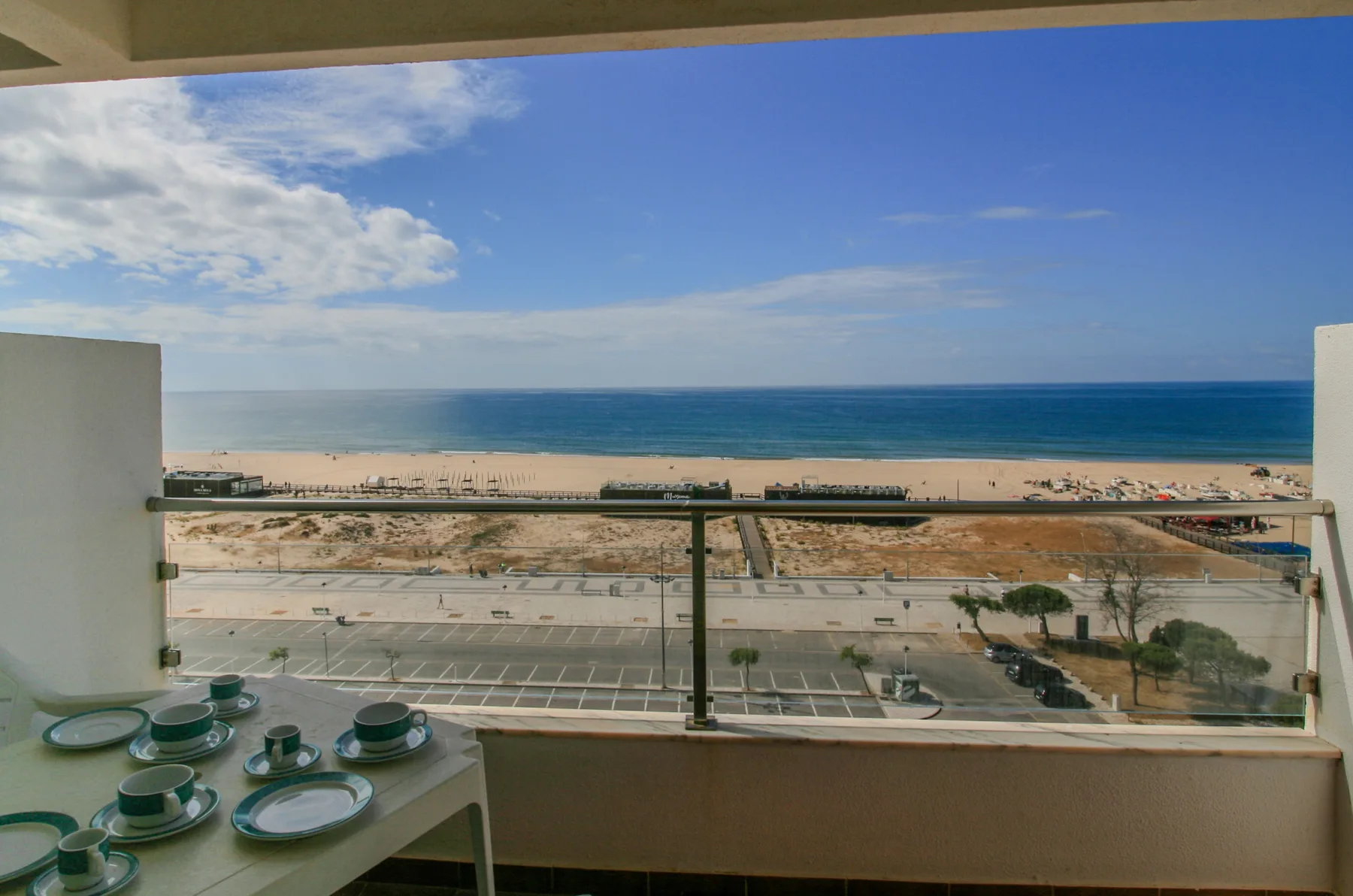 A balcony overlooks the beach and ocean beneath a partly cloudy sky.