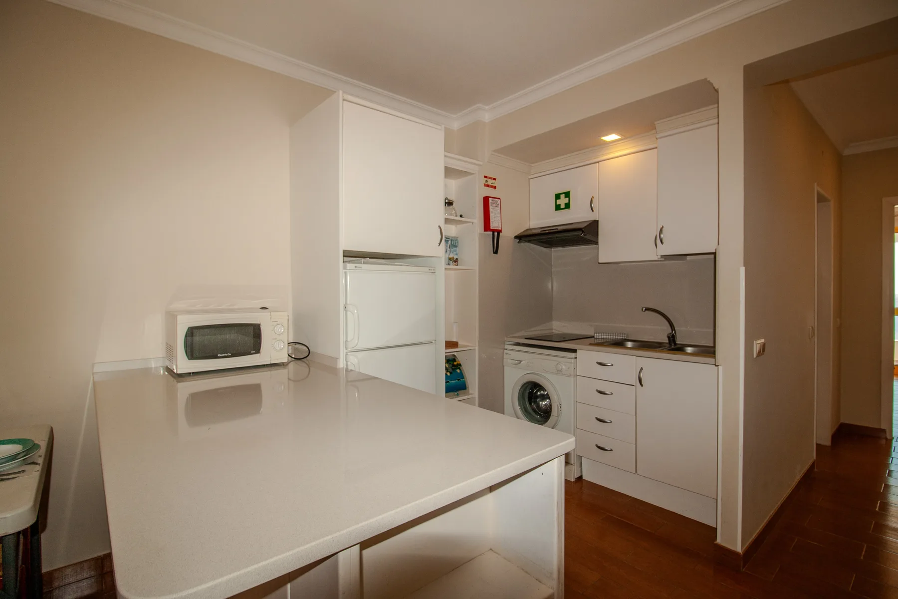 A compact kitchen with white cabinets, a countertop, and laundry appliances.