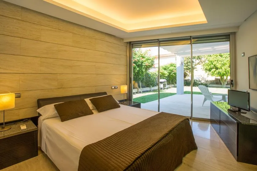 Un dormitorio con una cama doble frente a grandes puertas de vidrio y un jardín.