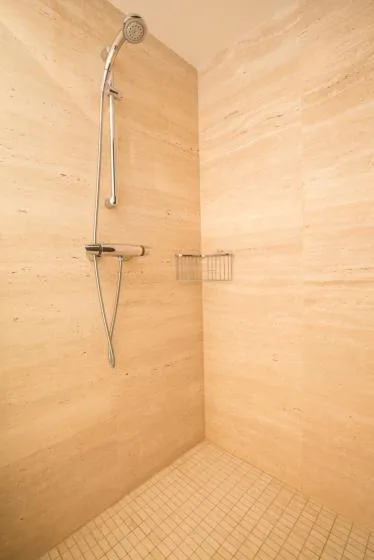 Una ducha revestida de azulejos con ducha de mano y controles en la pared.