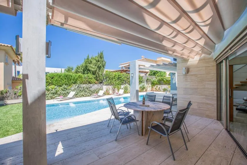 A shaded outdoor dining area overlooks a swimming pool and landscaped garden.