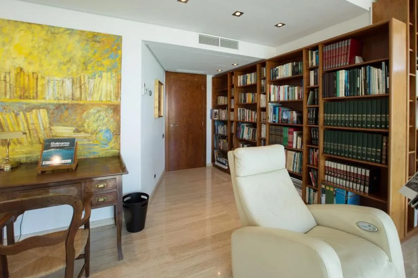 Una biblioteca con estanterías altas, un escritorio de madera y un sillón reclinable color crema.