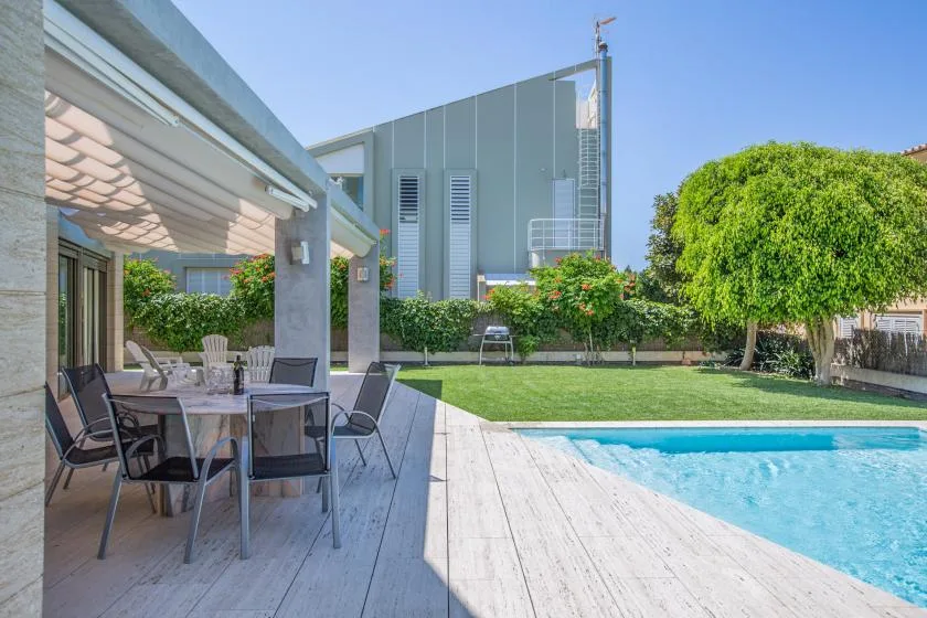Un patio al aire libre con asientos junto a una piscina y un jardín.