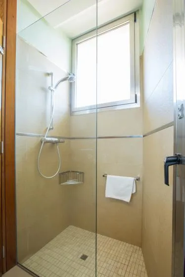 Una ducha con azulejos, una alcachofa de pared y una ventana luminosa.
