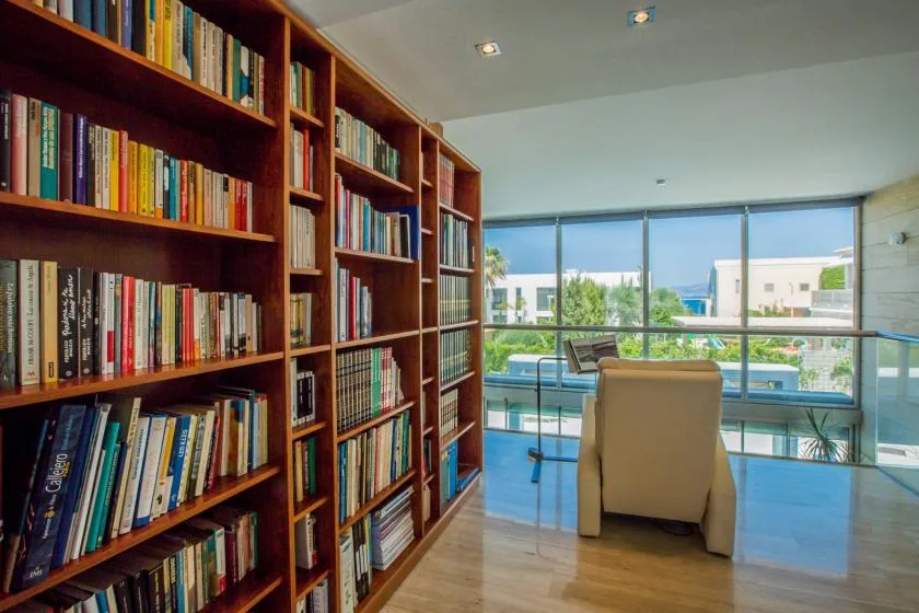 Un estudio con estanterías altas y un escritorio junto a grandes ventanales.