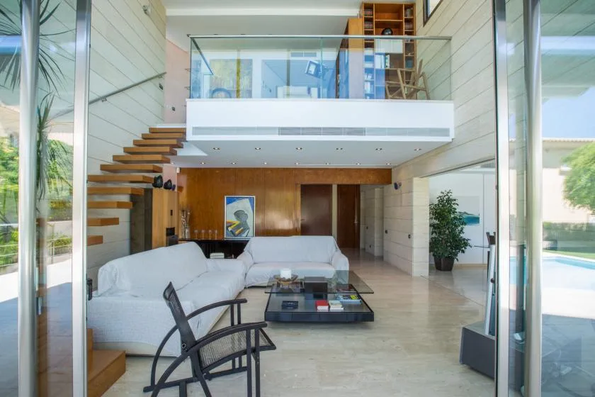 Una sala luminosa con asientos blancos, una mesa de centro de vidrio y una escalera abierta.