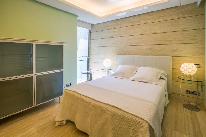 Un dormitorio con una cama grande, mesas auxiliares e iluminación cálida en el techo.