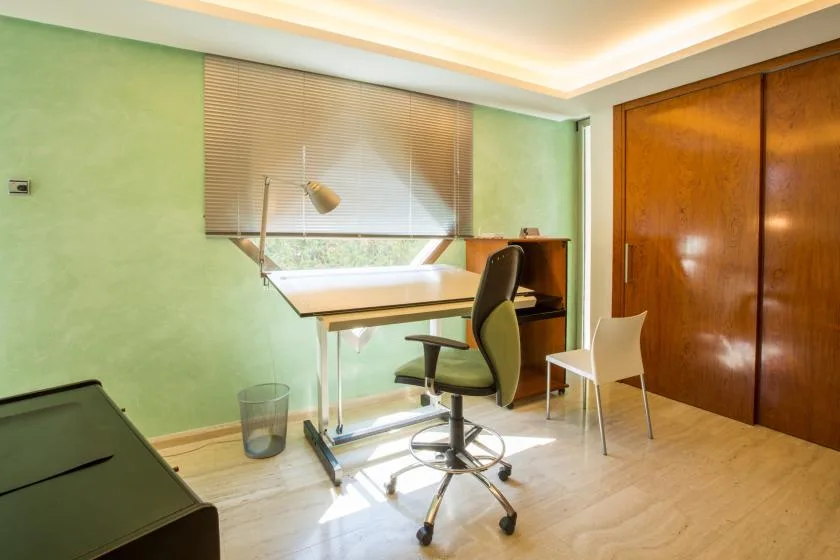 Un despacho en casa con escritorio, silla de oficina y una ventana con persianas.