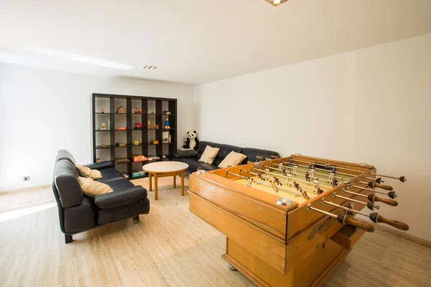 Una sala de juegos con futbolín, asientos y una estantería.
