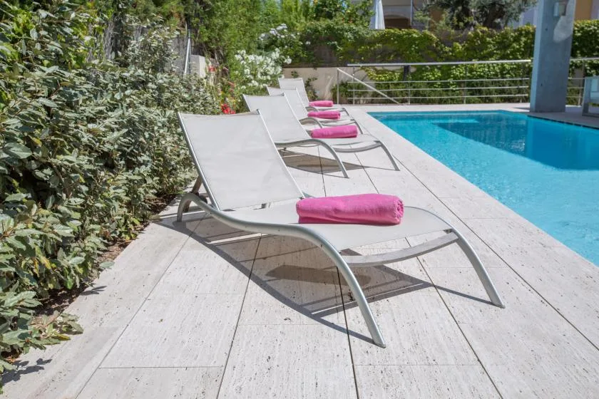 Un patio junto a la piscina con tumbonas y toallas rosas junto al agua.