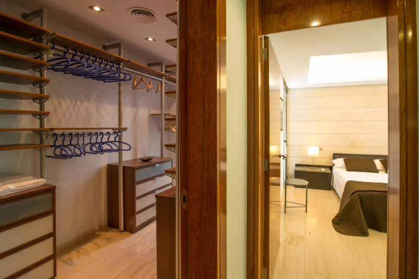Un vestidor con barras para colgar da a un dormitorio con cama y escritorio.