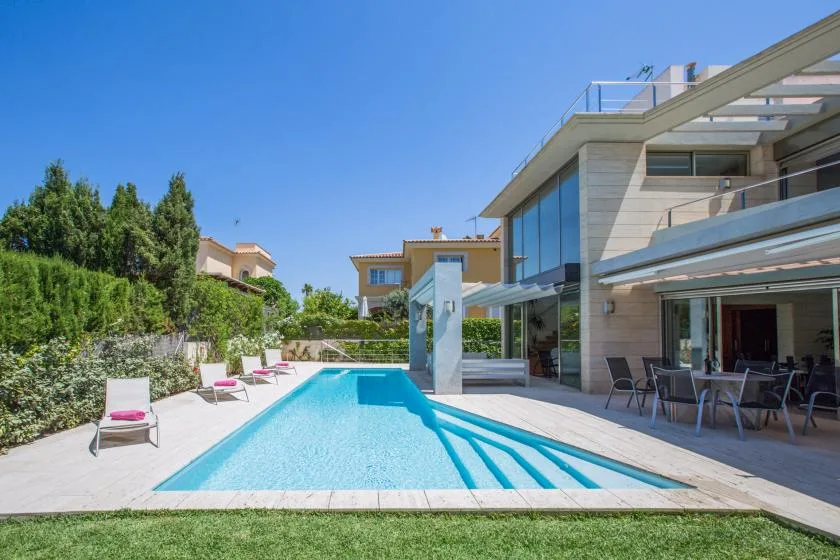 A modern house borders a swimming pool and patio under a clear sky.