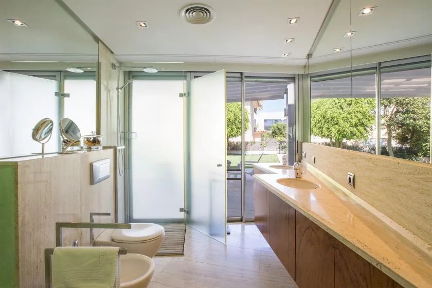 Un baño luminoso con un tocador largo, lavabos y una vista abierta a la vegetación.