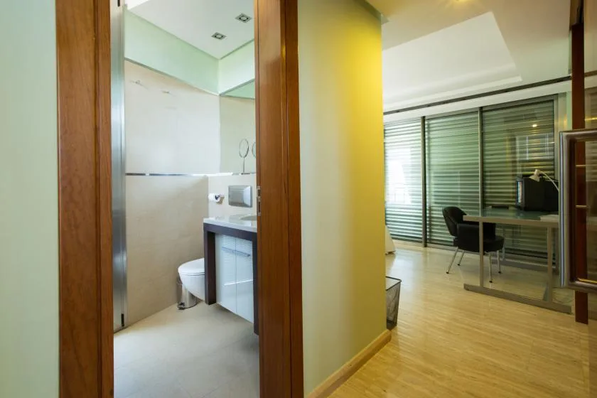 Un baño da a una habitación luminosa con escritorio y asientos.
