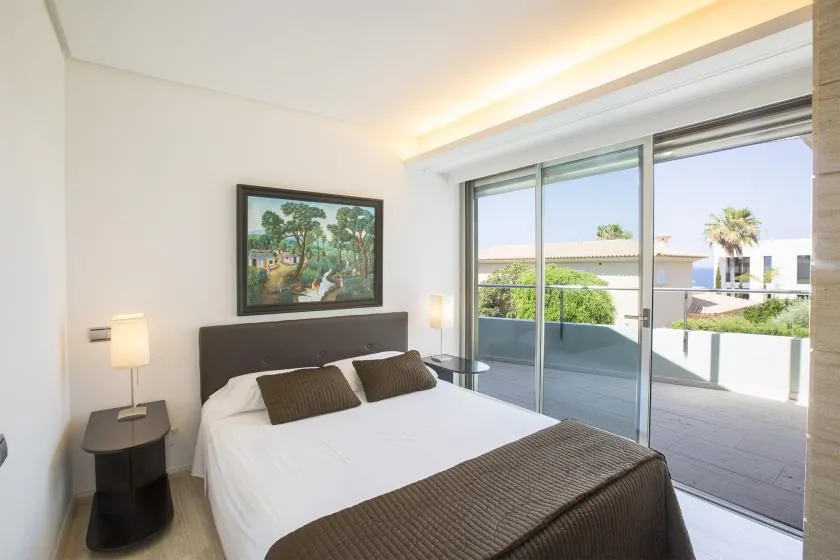 Un dormitorio luminoso con una cama tendida junto a grandes puertas corredizas de vidrio.