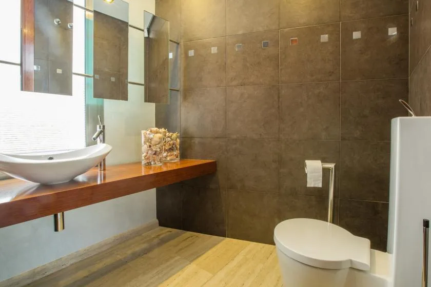 Un baño moderno con lavabo sobre encimera, inodoro y paredes de azulejos oscuros.