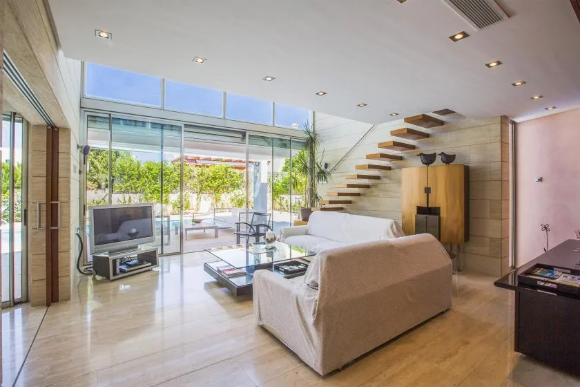 Una luminosa sala de estar con asientos, un televisor y grandes puertas de vidrio hacia un patio.