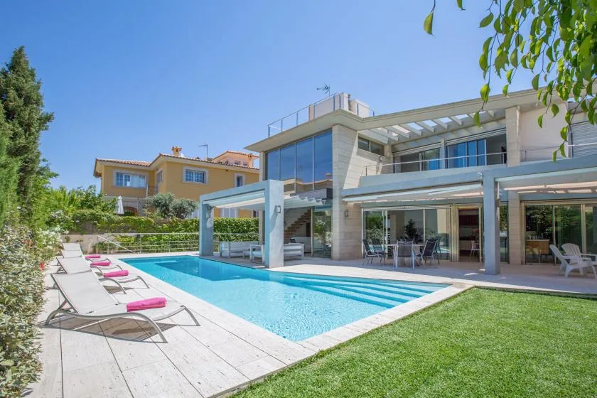 Una piscina junto a una casa moderna, con tumbonas en el patio.