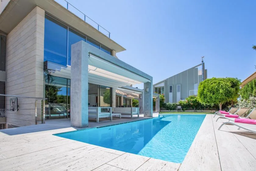 A swimming pool beside a modern building, with lounge seating along the deck.