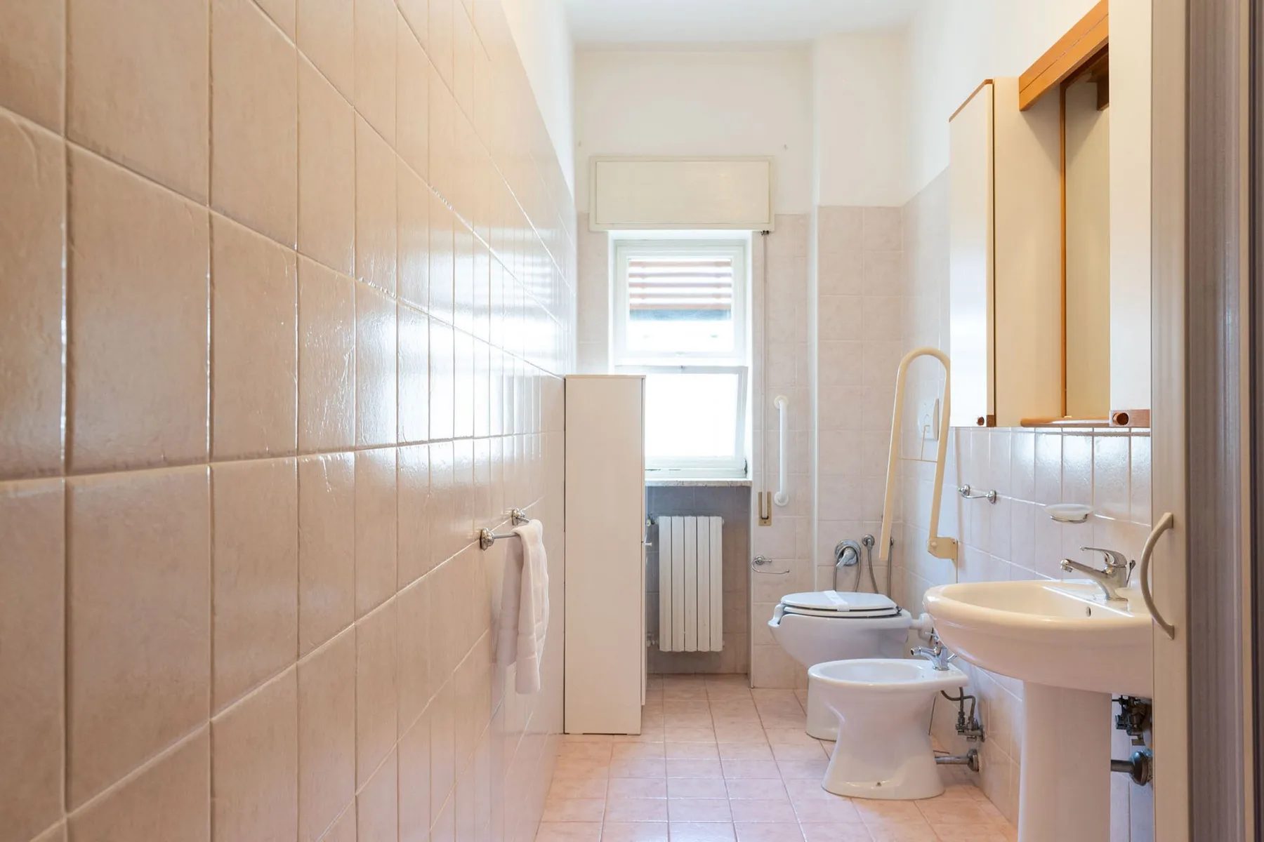 A tiled bathroom with a window, sink, toilet, and bidet.