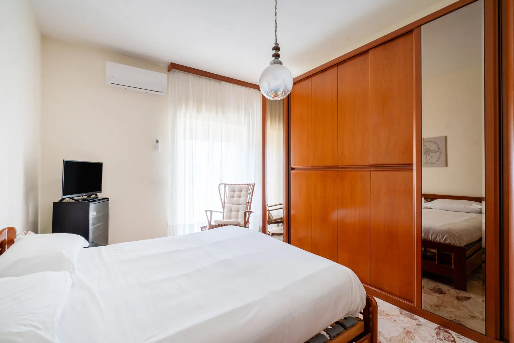 A bright bedroom with white bedding, a television, and wood-paneled wardrobes.