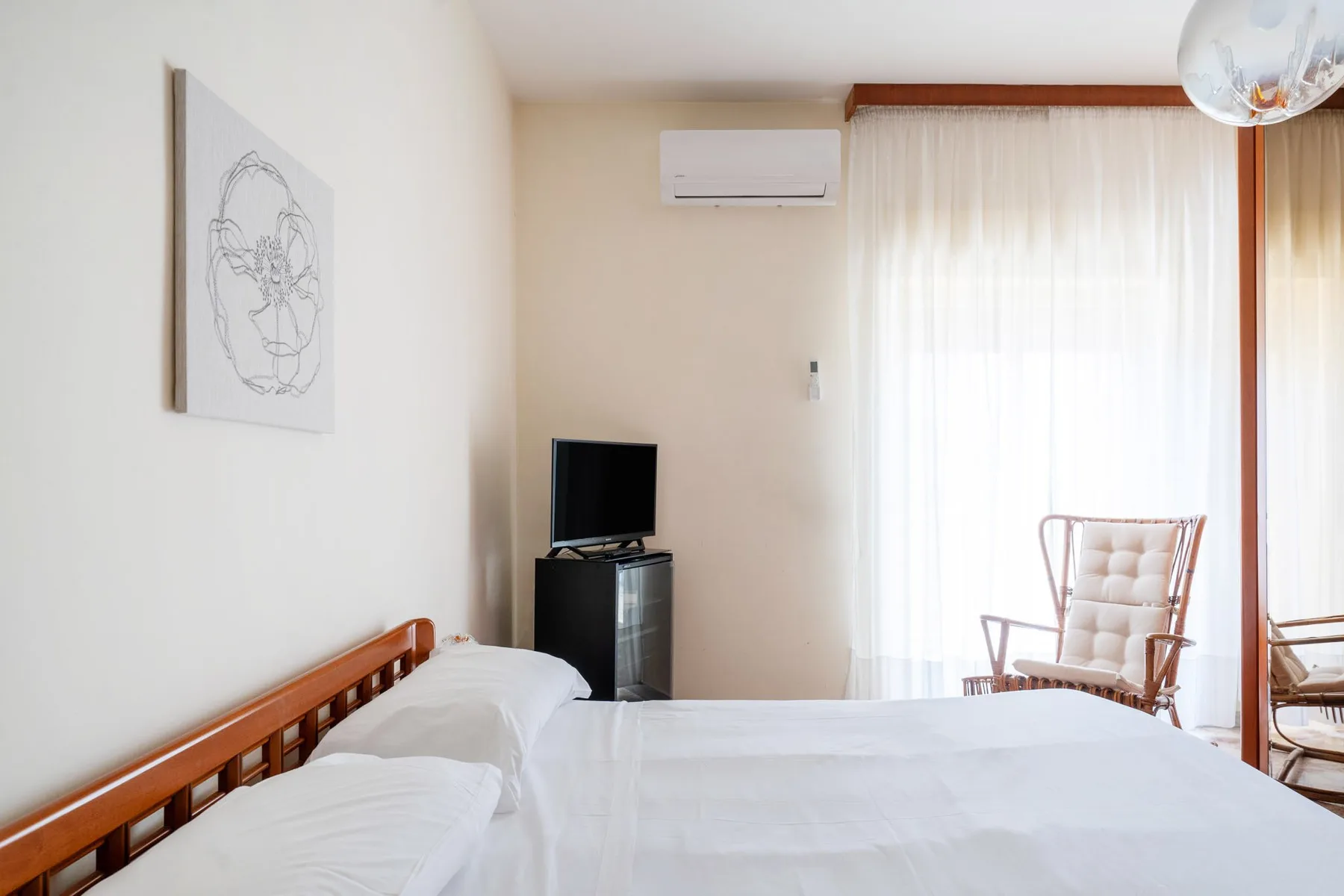 A bedroom with a bed, a small television, and a bright curtained window.