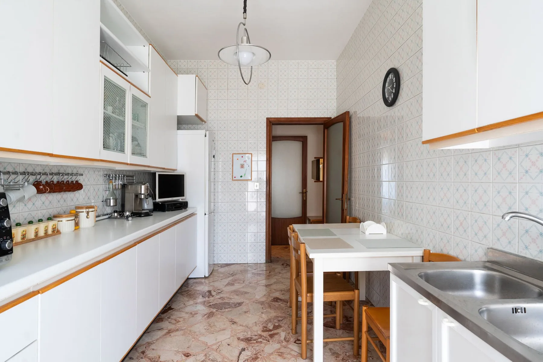 A tiled kitchen with white cabinets, a dining table, and a sink.
