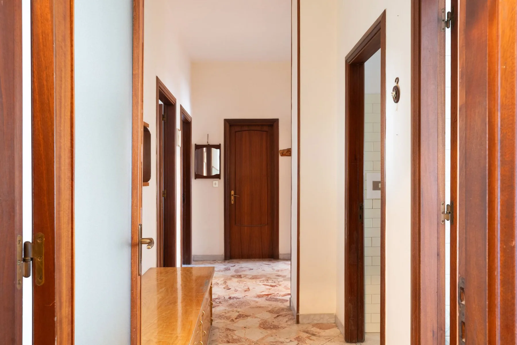 A hallway with wooden doorways and a patterned tile floor.