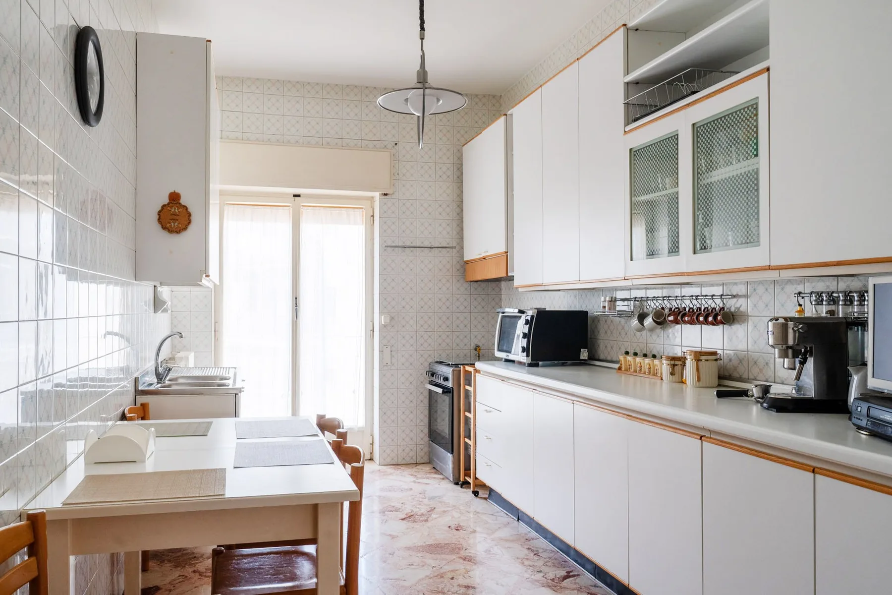 A bright kitchen with white cabinets, a long counter, and a small dining table.
