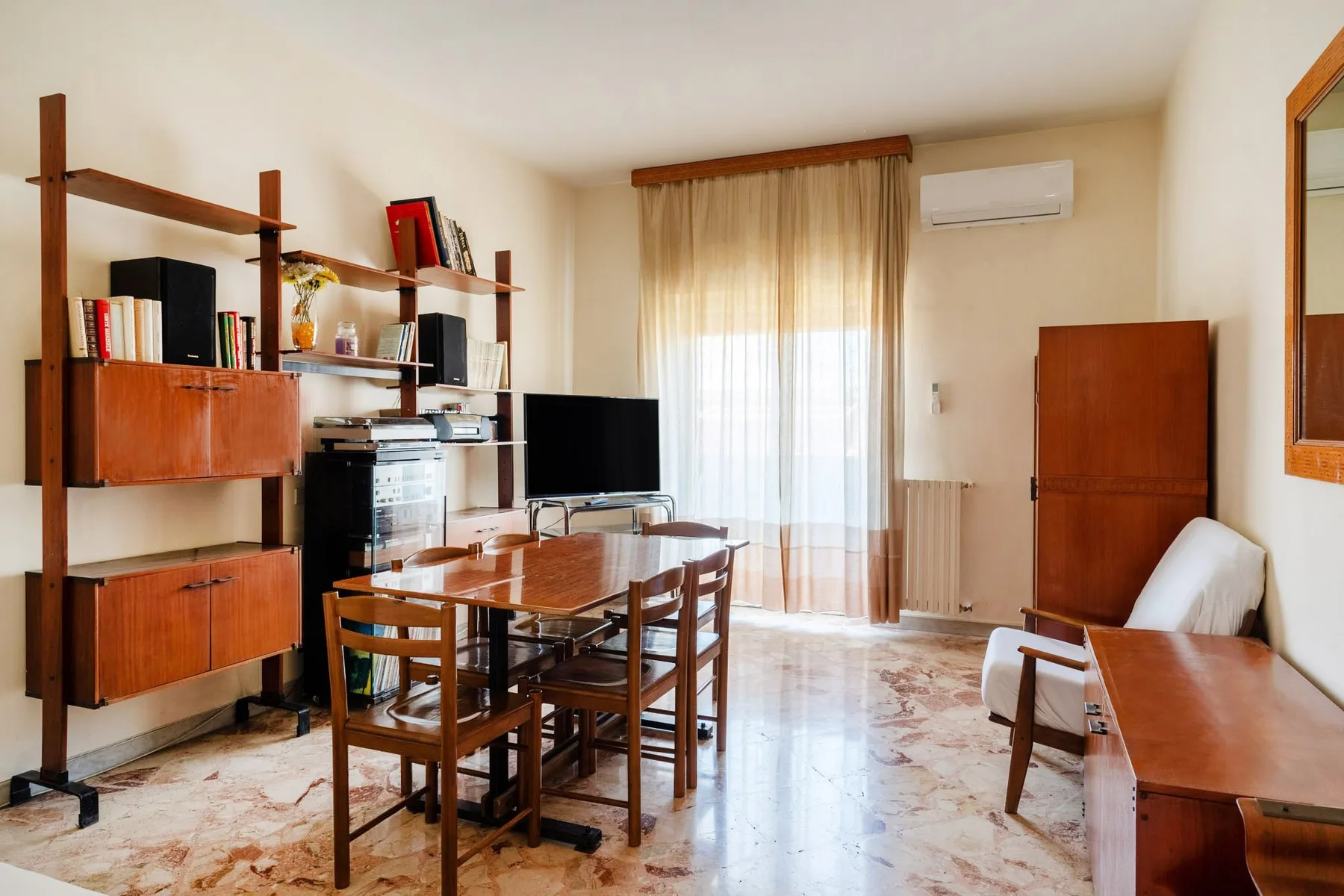 A living and dining room with a wooden table, seating, and shelving.