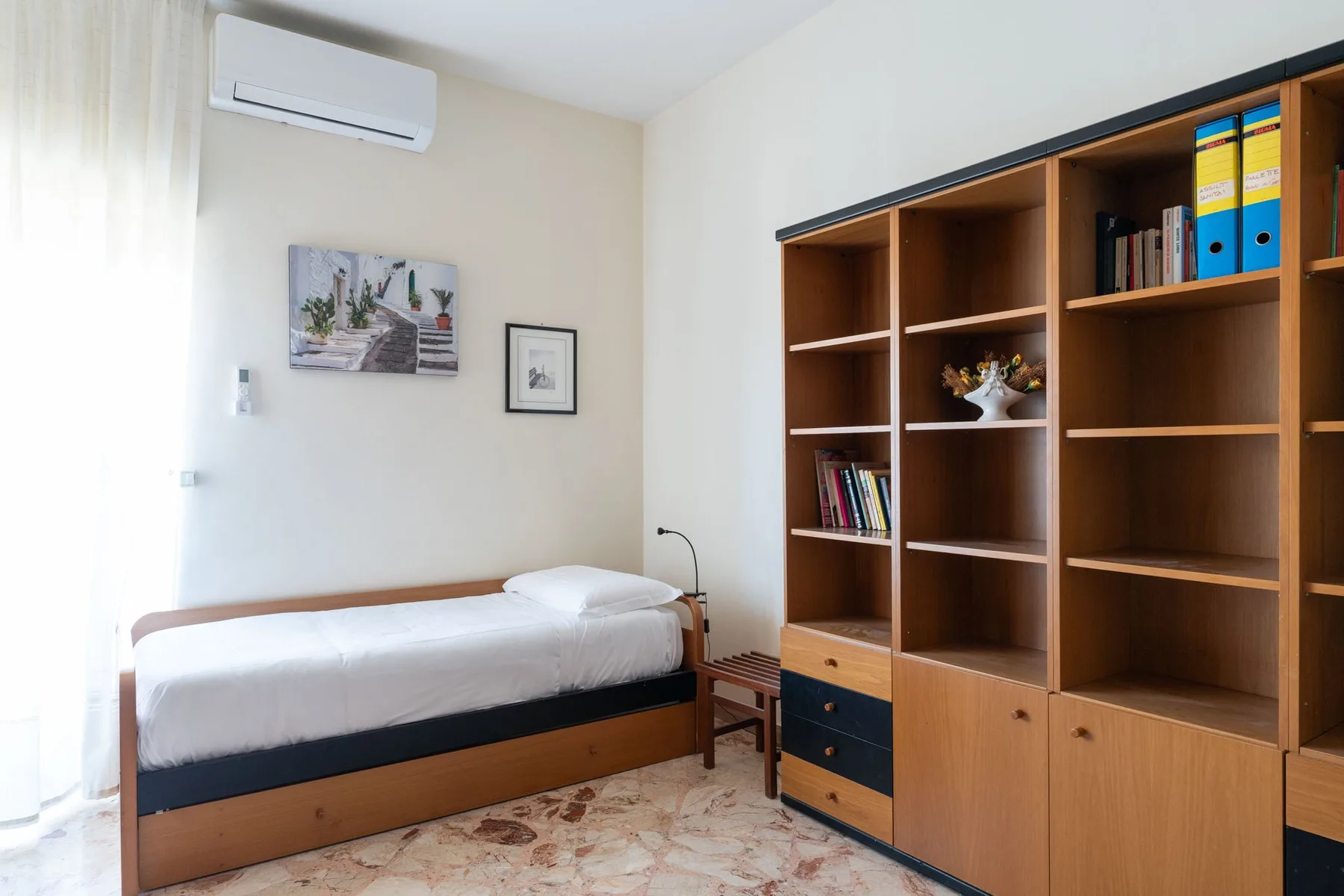 A bedroom with a single bed beside a wooden shelving unit.