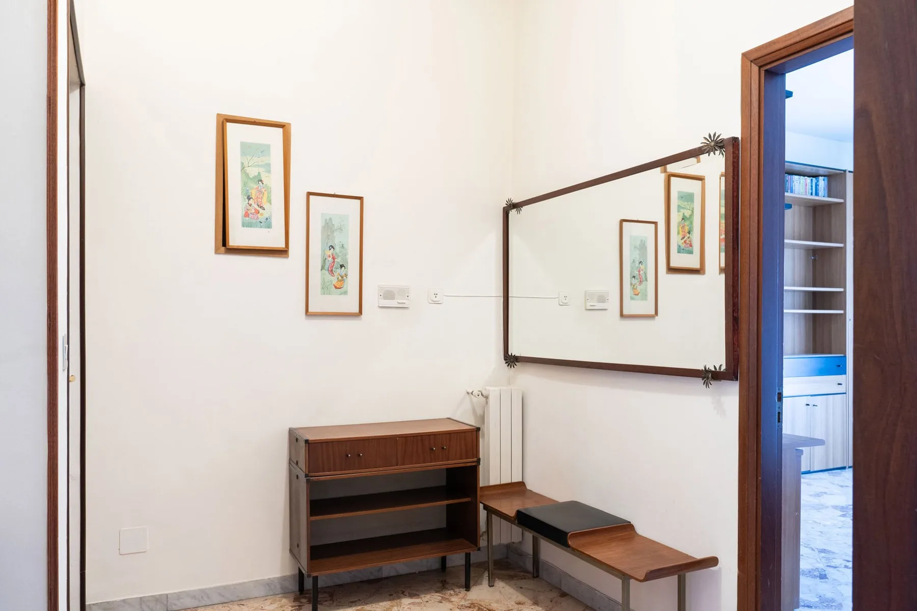 A bright entry area with a wall mirror, framed artwork, and a small bench.