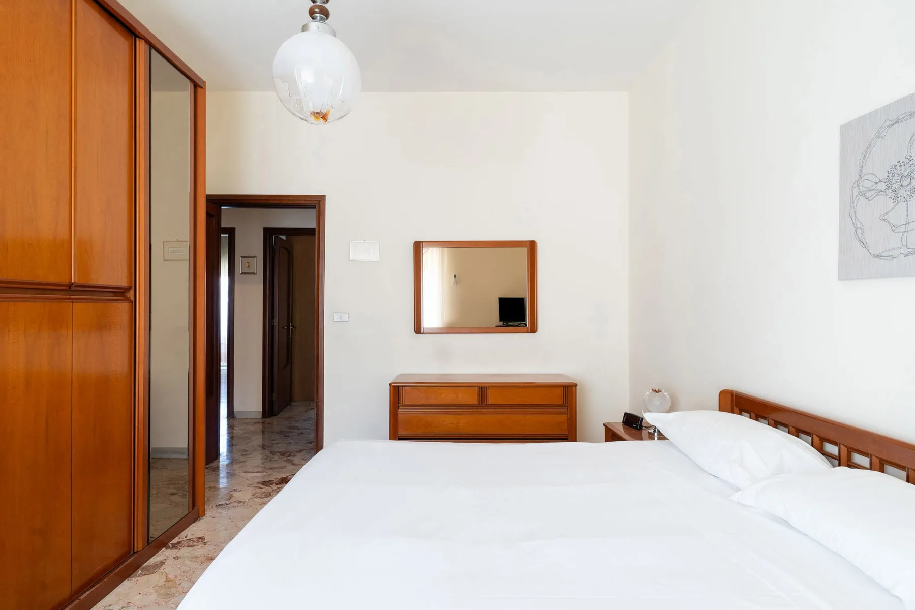 A bedroom with a large bed, wooden wardrobe, and dresser.