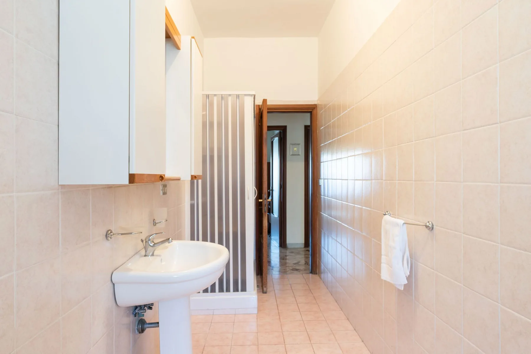 A tiled bathroom with a sink and shower beside a hallway doorway.