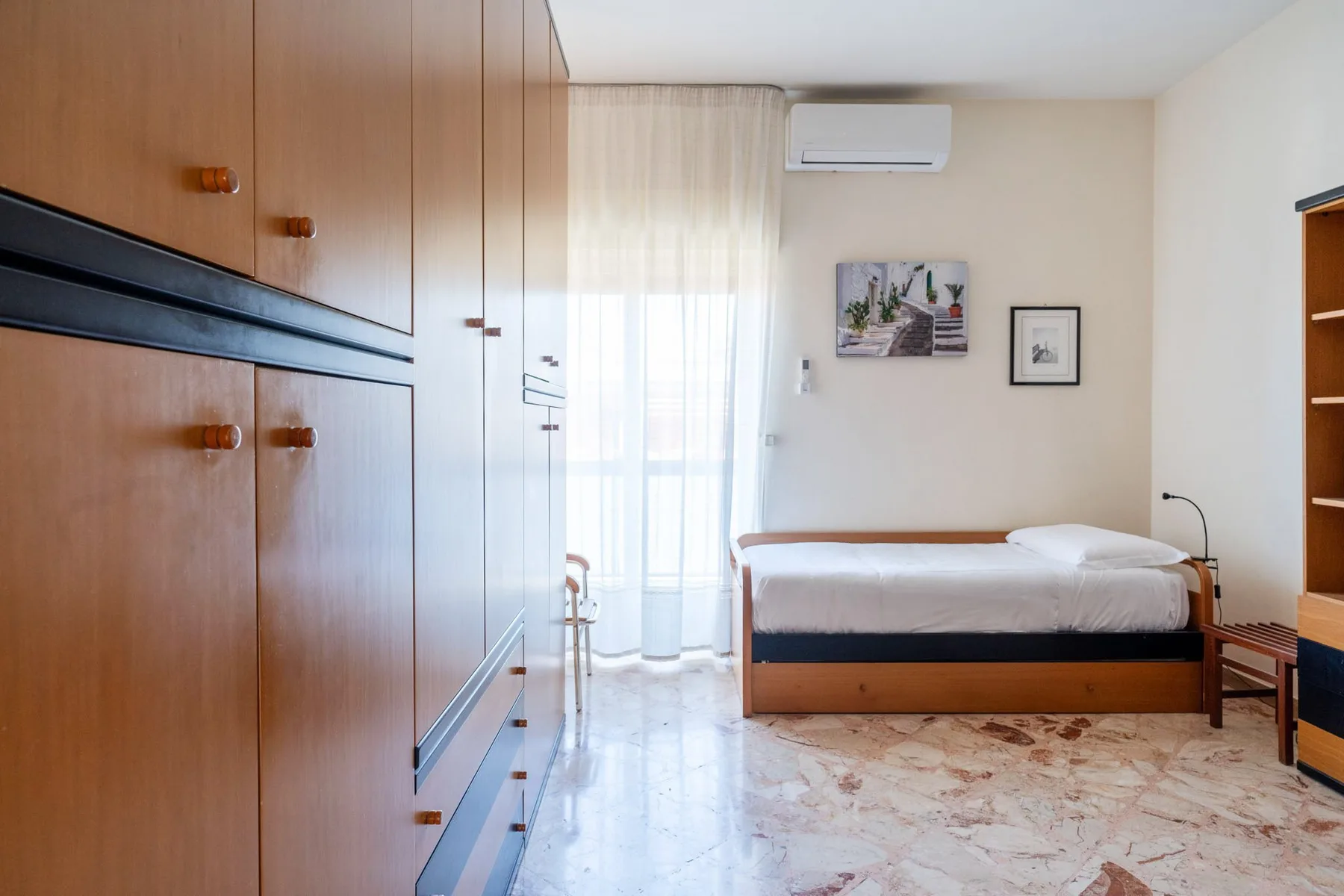 A bedroom with a single bed, built-in wardrobes, and a bright window.