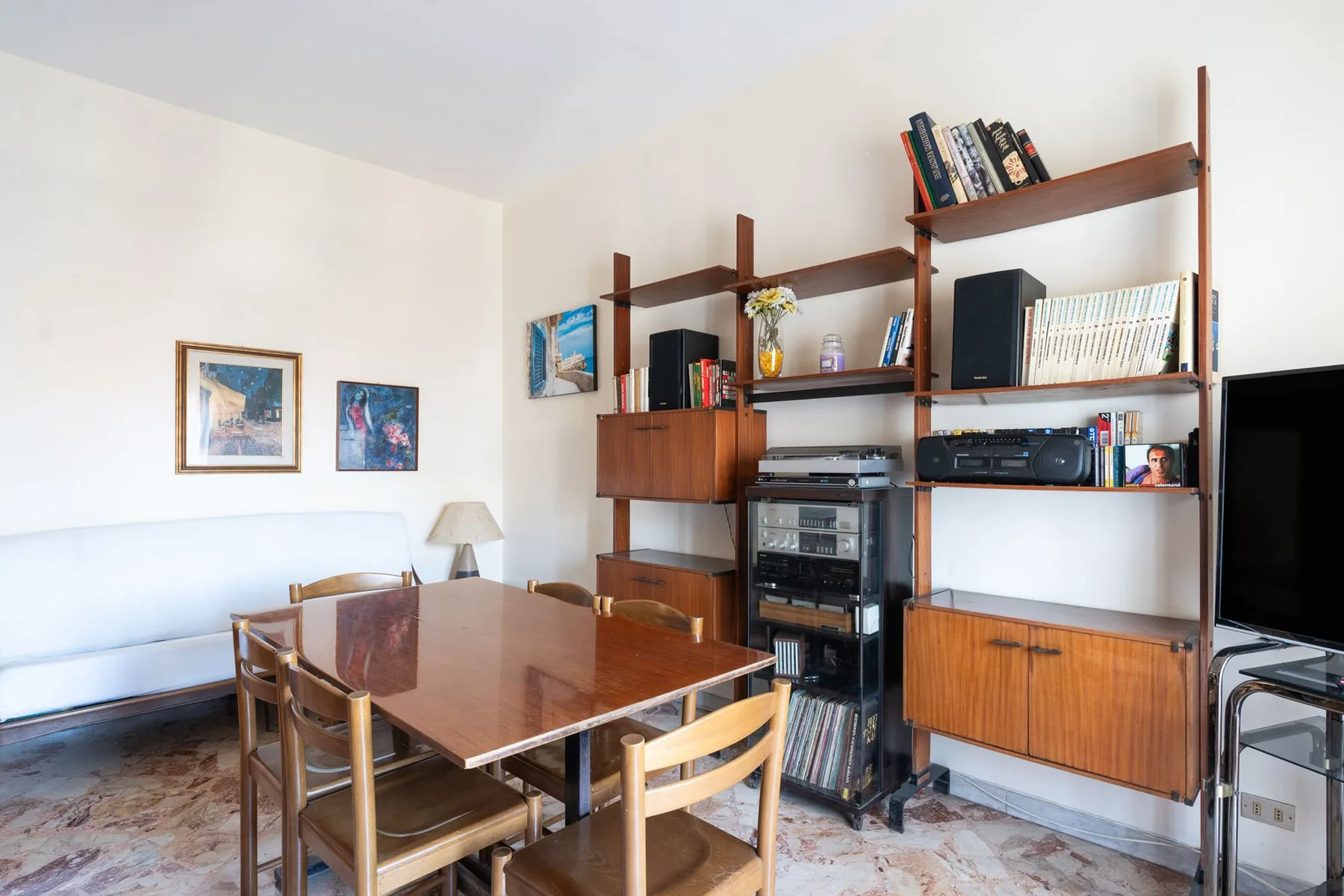 A dining area with a wooden table and shelving along the wall.