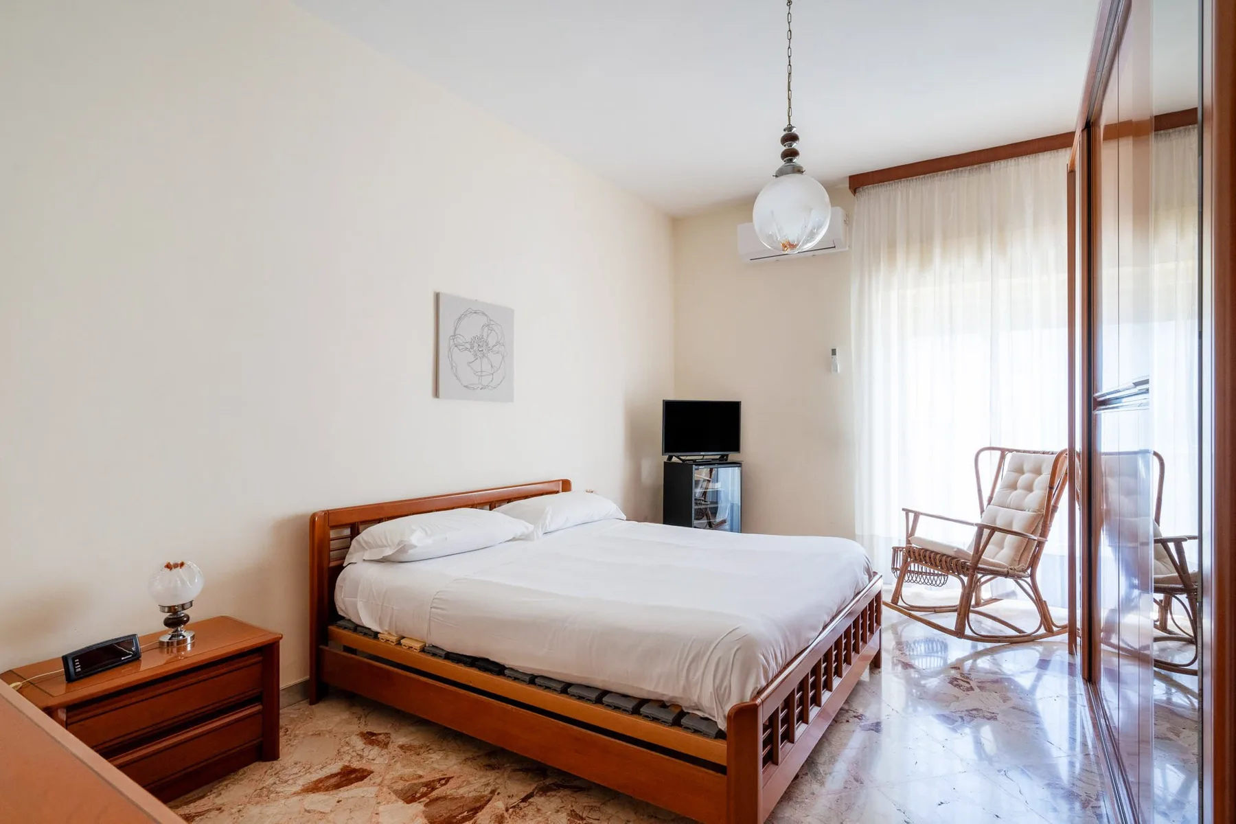 A bright bedroom with a wooden bed and a rocking chair beside the window.