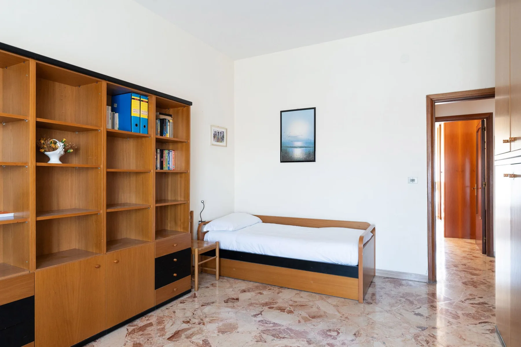 A bedroom with a single bed, wooden shelving, and an open doorway.