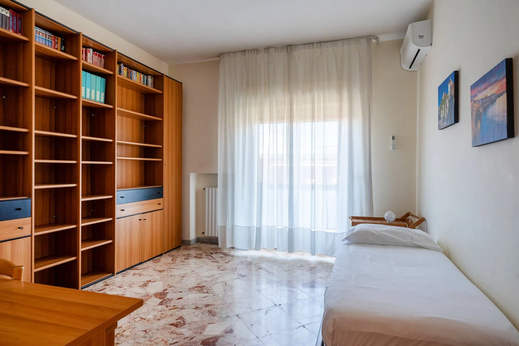 A bedroom with a single bed, built-in shelving, and a curtained window.