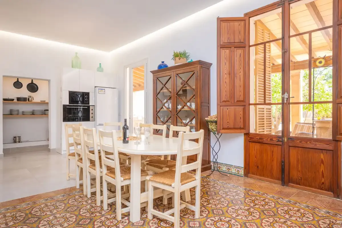 Un comedor luminoso con una mesa larga junto a armarios de madera y ventanas.