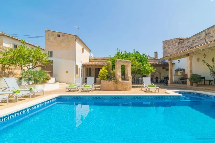 Una piscina está en un patio soleado con asientos al aire libre y edificios alrededor.