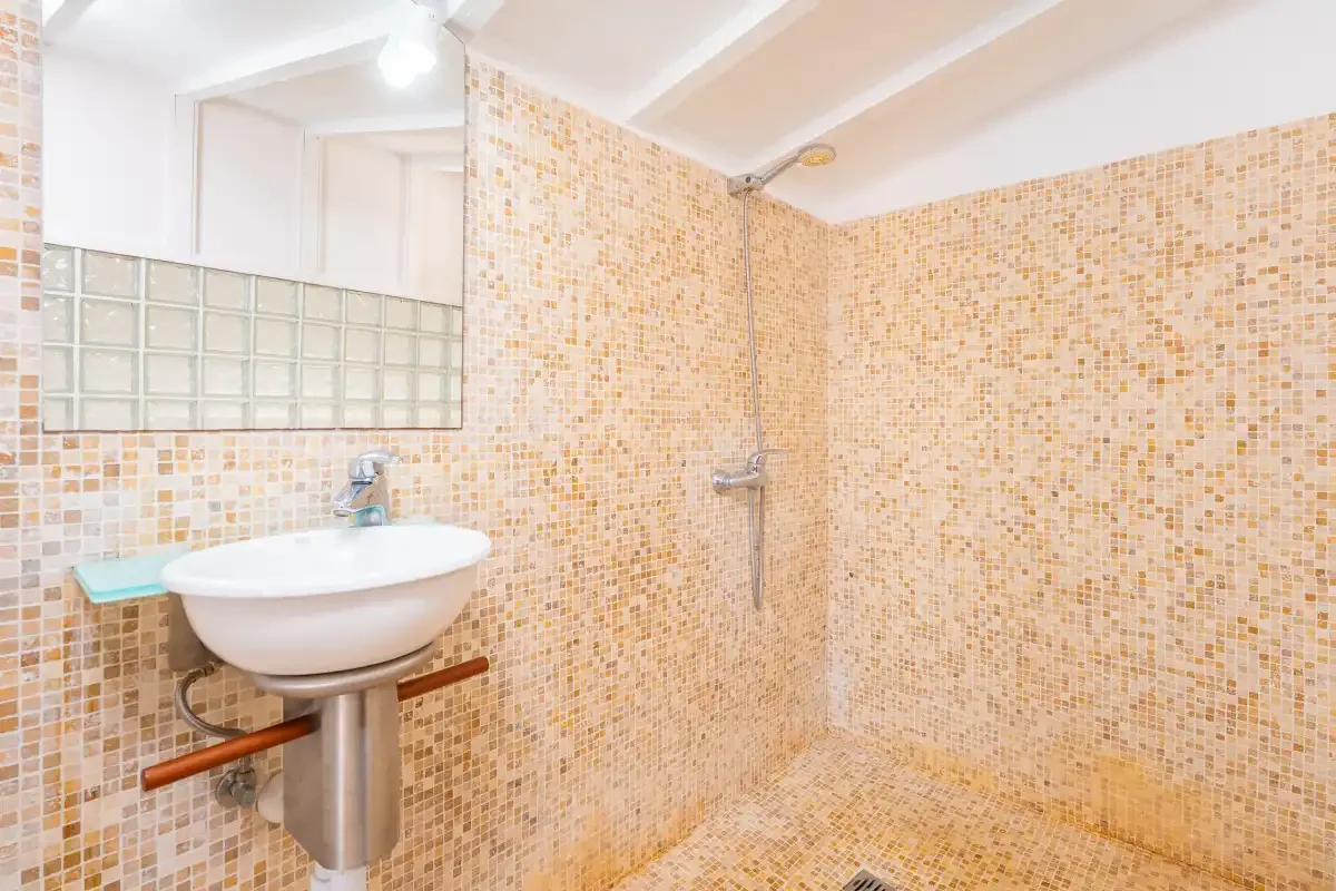 Un baño alicatado con lavabo de pared y ducha.