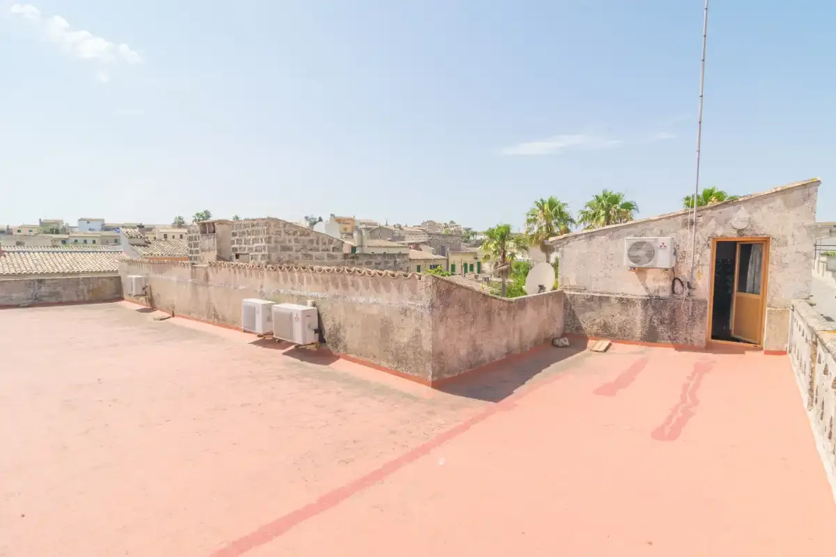 Una terraza soleada en la azotea, con muros bajos y una puerta.