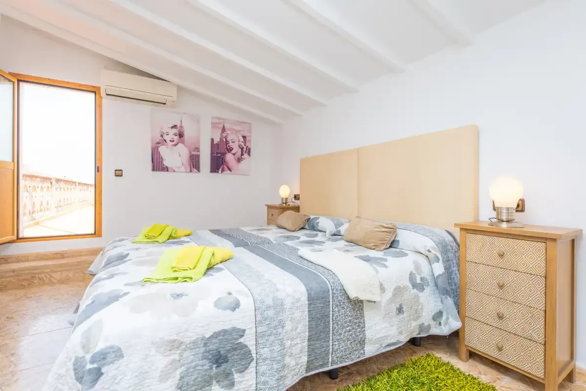 Un dormitorio luminoso con una cama doble, lámparas de noche y una ventana.