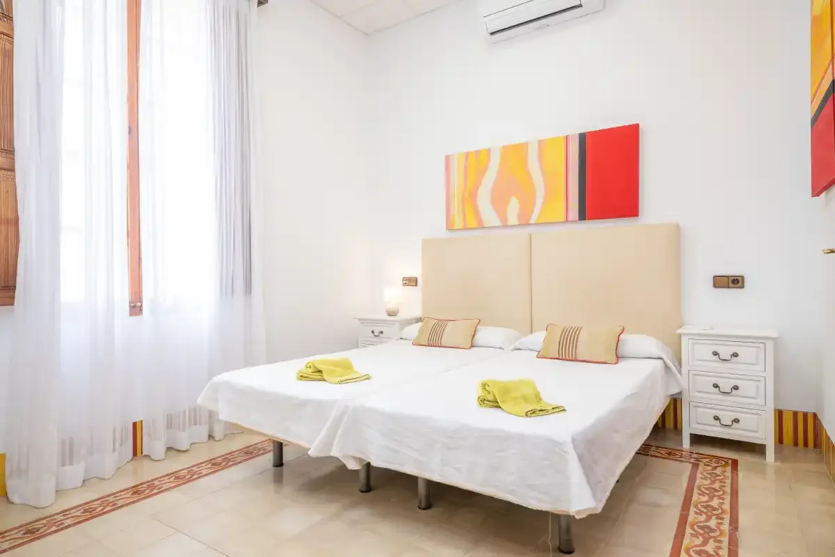 Un dormitorio luminoso con una cama doble, mesitas de noche y arte colorido en la pared.