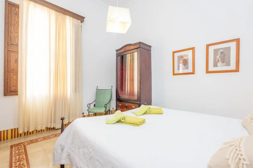 Un dormitorio con una cama tendida, un armario de madera y una silla.