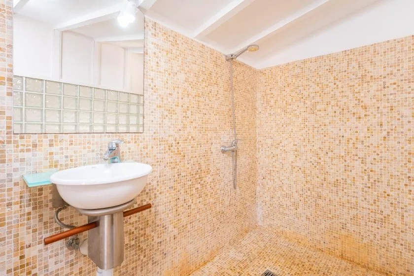 Un baño con azulejos, lavabo con pedestal y accesorios de ducha.